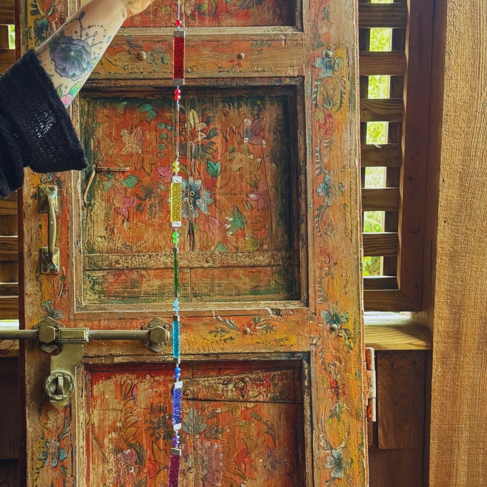 Rainbow stained glass sun catcher hanging in front of a vintage wooden door, colorful prism window decor for boho home styling.