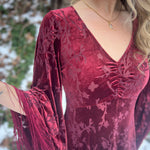 Red velvet dress with floral patterns and fringes on a blurred natural background