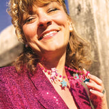 Woman wearing a sparkly pink jacket with a colorful necklace, standing outdoors.