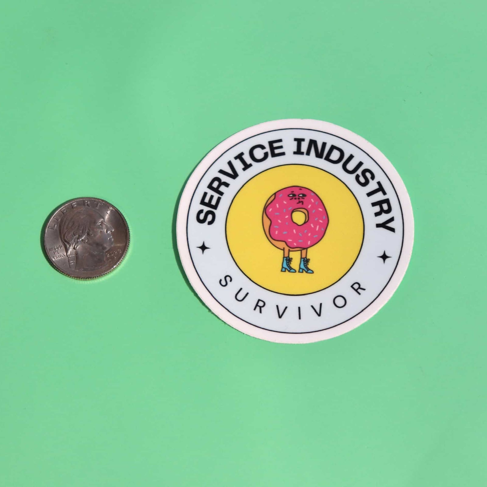 The Service Industry Restaurant Humor Sticker next to a quarter on a green background.