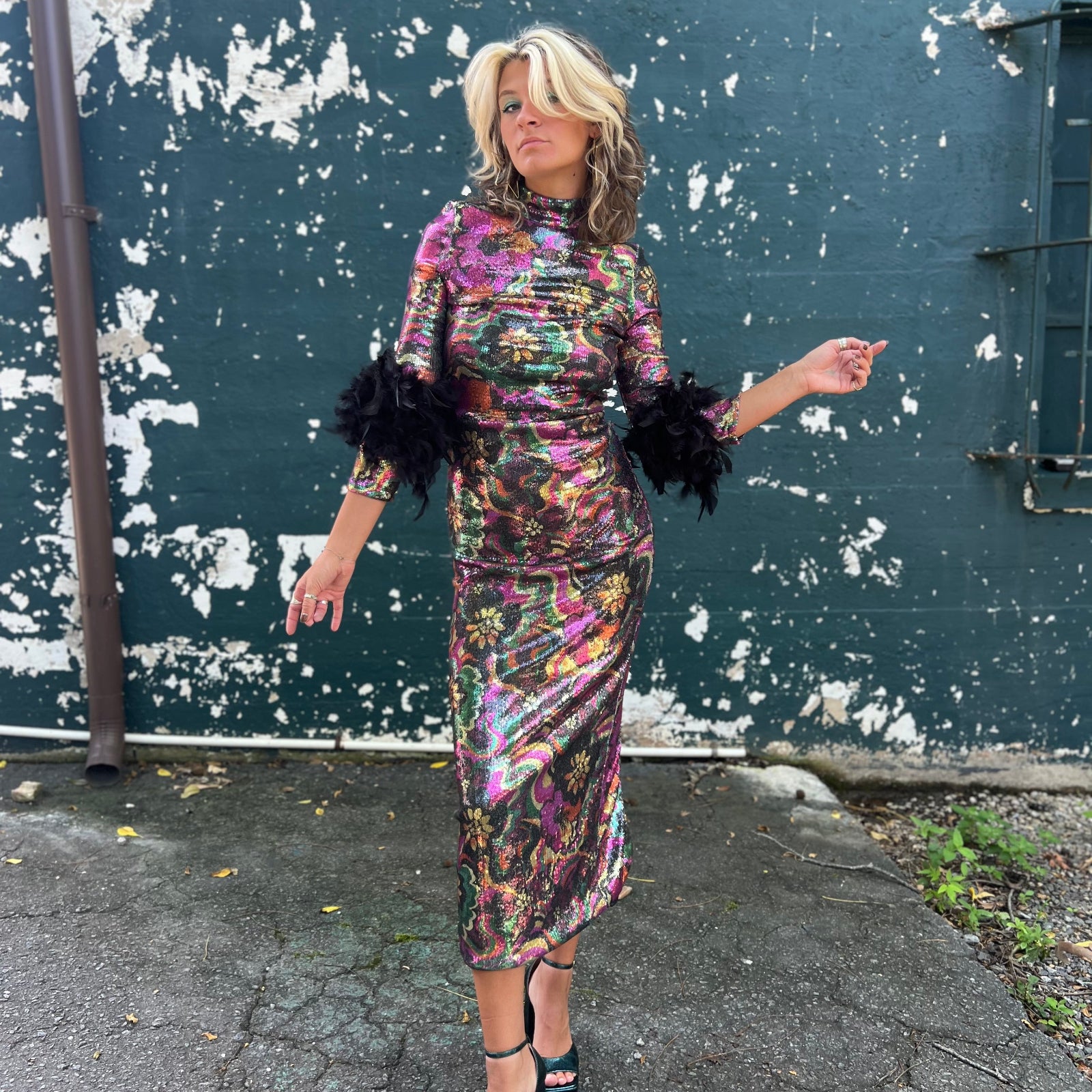 Woman in a floral dress with black sleeves against a textured wall.