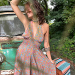 Woman in a floral dress sitting next to a vintage car with greenery in the background