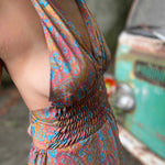Woman wearing a colorful dress with fringe details, standing next to a vintage scooter.