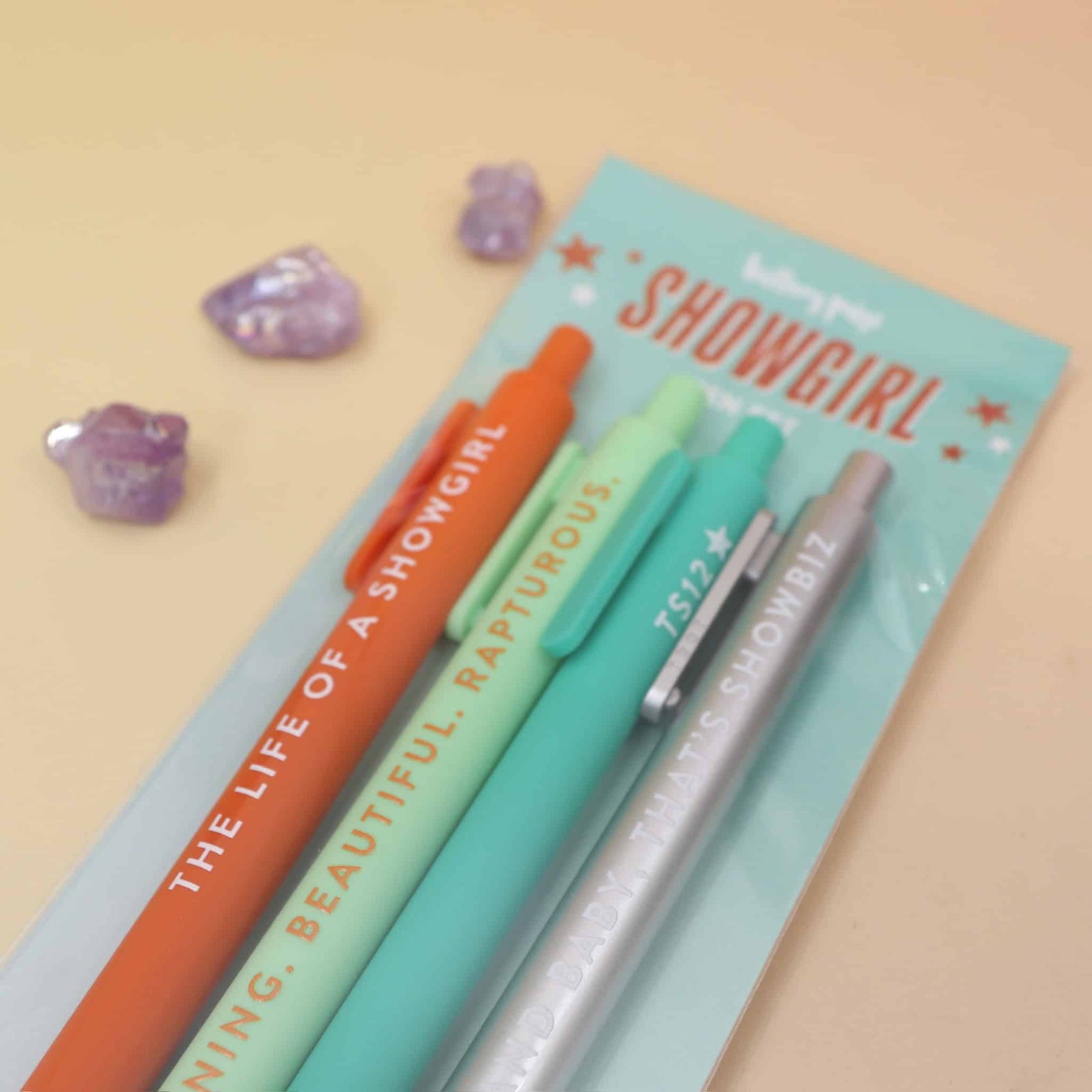 Set of pens with Taylor Swift Life of a  'Showgirl' branding on a pastel blue card against a beige background.