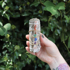 Hand holding a crystal wand with colorful stones against a green leafy background