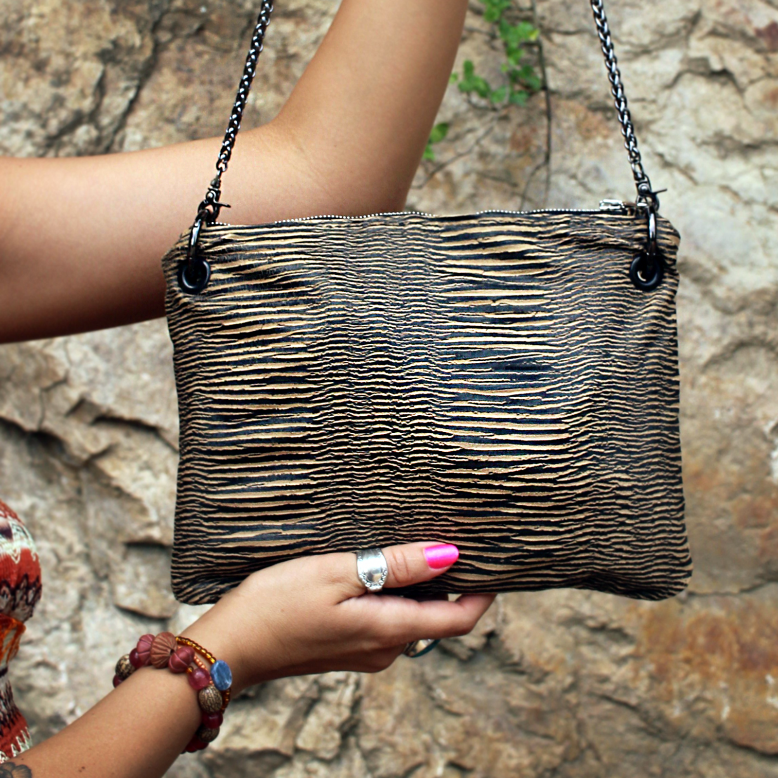 Someone holding the Distressed Black and Tan Bengal Stripe Crossbody Bag in front of a stone wall.